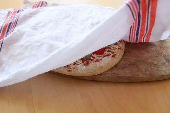 a frozen pizza being covered by a wet kitchen towel