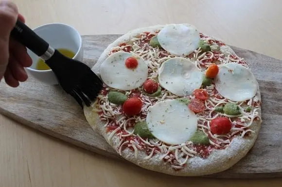 olive oil being brushed onto a frozen pizza