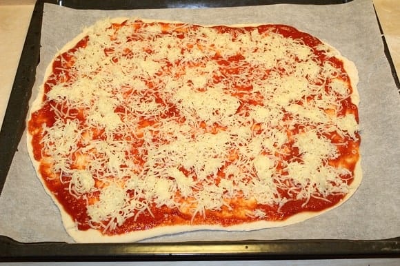 an unbaked homemade pizza on a baking sheet ready for the oven