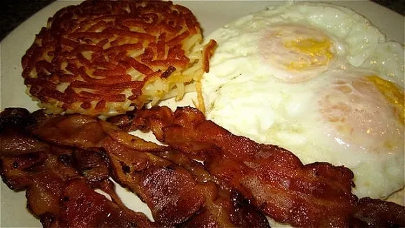 a hash brown, some bacon, and eggs on a dinner plate