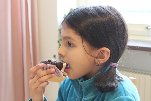 a little girl eating a chocolate muffin with a partically unwrapped wrapper