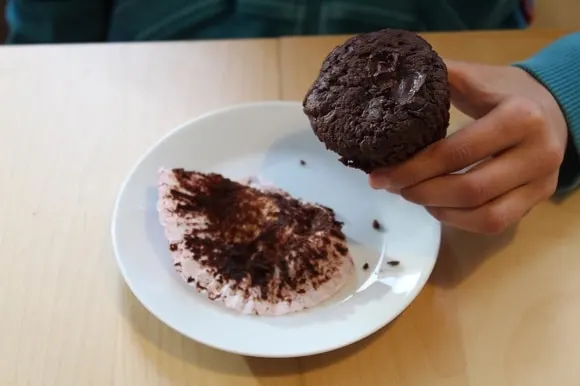 a little girl holding an unwrapped chocolate muffin