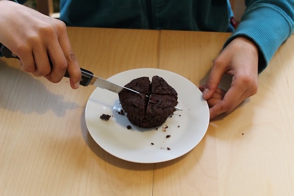 a little girl cutting a muffin into four equal pieces with a knife