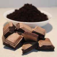 several pieces of 70% dark chocolate in front of a bowl filled with black cocoa powder