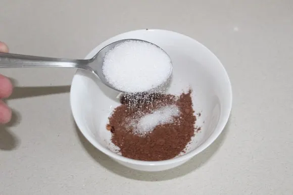 white sugar being added to unsweetened cocoa powder
