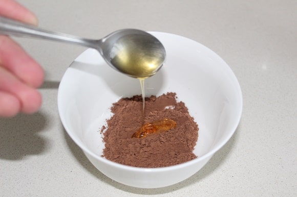 a teaspoon of agave syrup being added to cocoa powder