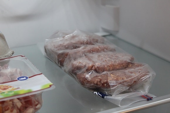 a pack of four frozen hamburtgers slowly thawing in the fridge