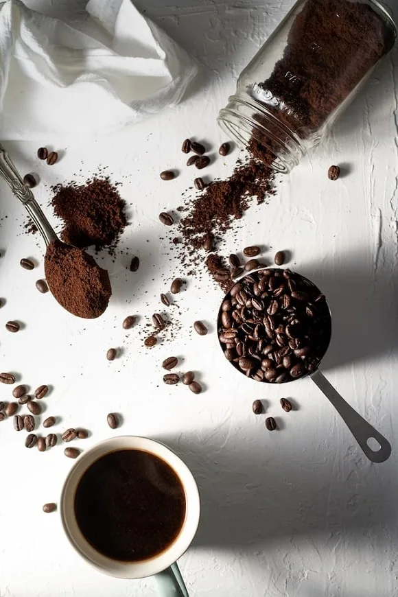a cup of coffee, coffee beans, and cocoa powder on a table