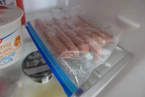 a pack of frozen hot dogs slowly thawing in the fridge