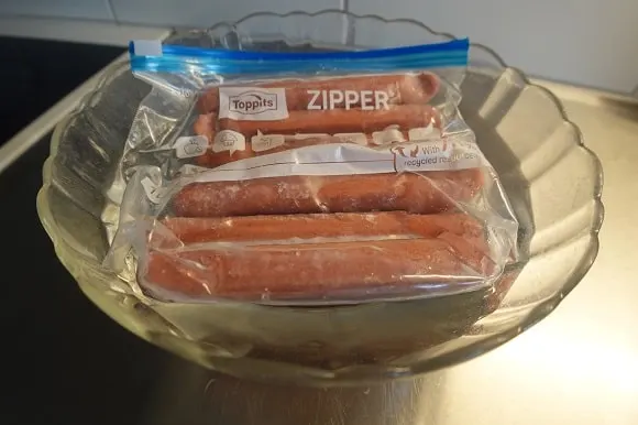 a pack of frozen hot dogs thawing in a bowl of cold water